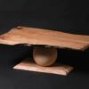 Le plateau de cette table en noyer présente des lignes fluides avec des touches de laiton pour un look dynamique. Chaque courbe est sculptée pour donner vie au bois, qui semble presque bouger. La base, une sphère en peuplier, est tournée à la main avec précision et soutient le plateau. C'est une prouesse d'équilibre et d'artisanat, simple mais élégante.