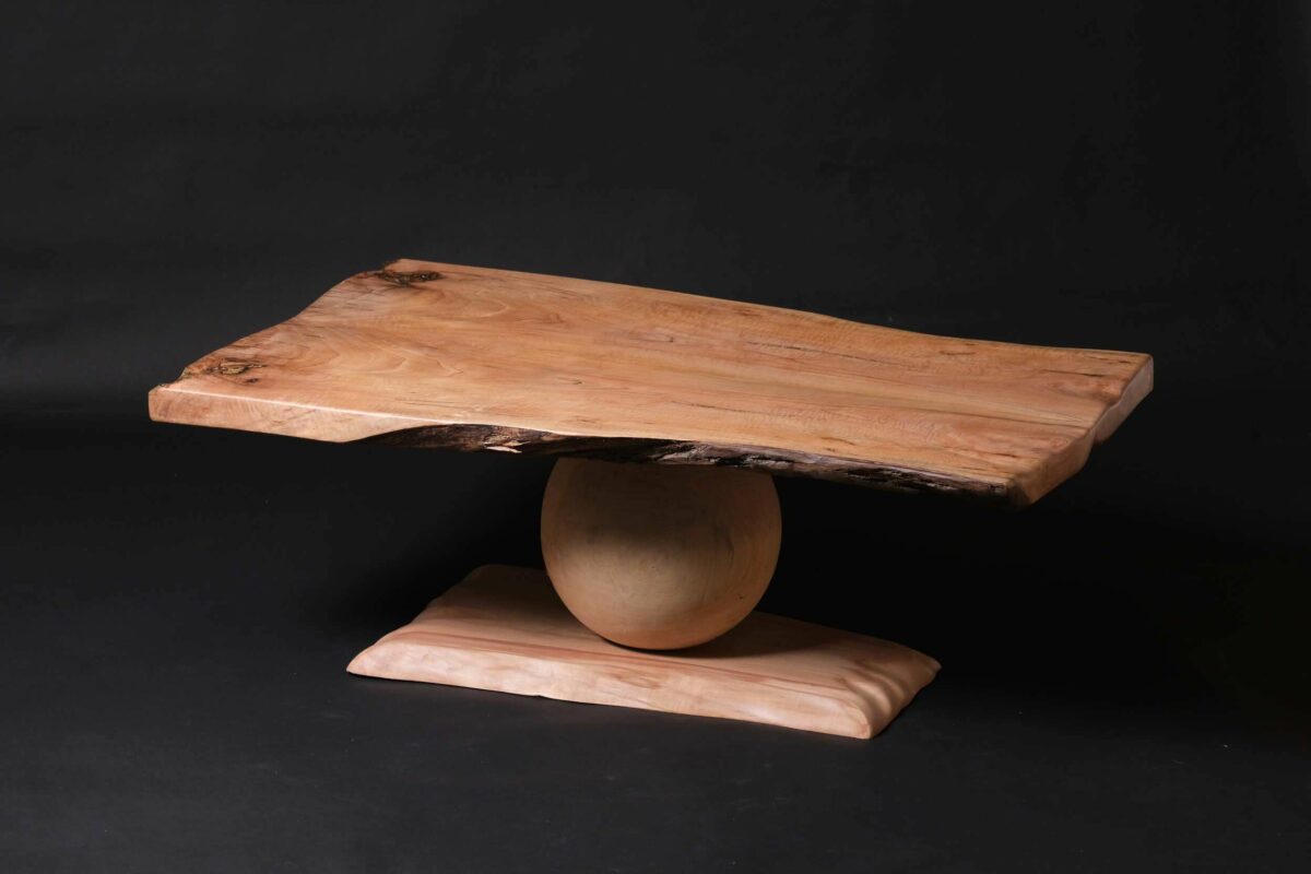 Le plateau de cette table en noyer présente des lignes fluides avec des touches de laiton pour un look dynamique. Chaque courbe est sculptée pour donner vie au bois, qui semble presque bouger. La base, une sphère en peuplier, est tournée à la main avec précision et soutient le plateau. C'est une prouesse d'équilibre et d'artisanat, simple mais élégante.